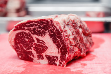 Obraz premium Closeup macro pieces ribeye marbled beef steak on red plastic cutting board on metal table in restaurant kitchen. Concept packing semifinished products, freezing food, steakhouse, grill meat