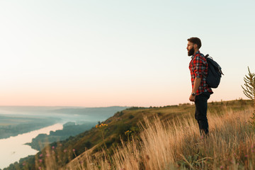 Hipster tourist with backpack on hillside