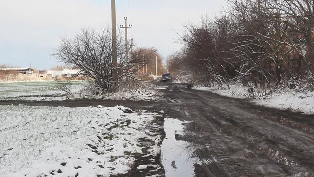 The car rides on a dirty bumpy road. Muddy road along the snow-covered fields