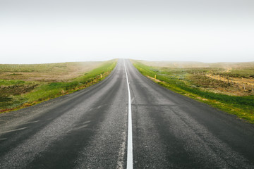 Straight country road on the hill among green fields on a foggy summer day. Minimalist landscape in Northeastern Region, Iceland