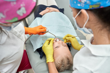 Stomatologists in medical caps curing kid's teeth.
