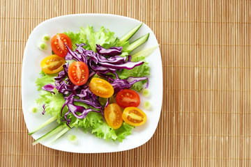 vegetable salad on a white plate, bamboo napkin, view from the top