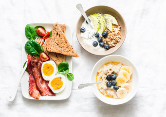 Varied sweet and savory breakfast - bacon with egg and vegetables, spinach salad, yogurt with granola and fruit, vegetarian oatmeal on a light background, top view