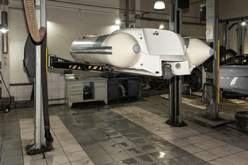 A small white rubber motorboat raised on a car lift for cleaning and repairs in a vehicle repair and maintenance workshop