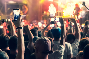 a crowd of people with raised hands shoots video on the phone at a street concert, blurred background