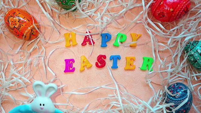 Two plates (pink and blue) with Easter bunny is placed next to painted multicolored Easter eggs, decorative straw and the words "Happy Easter" written in multicolored letters.