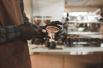 Background. Close-up photo of a barista in gloves holds a portafilter of coffee. Holder with coffee in the hands of Barista.