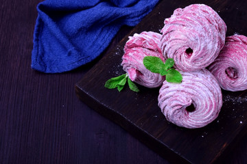 Berry zephyr covered in sugar powder on a black wooden board