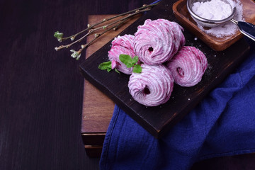 Berry zephyr covered in sugar powder on a black wooden board