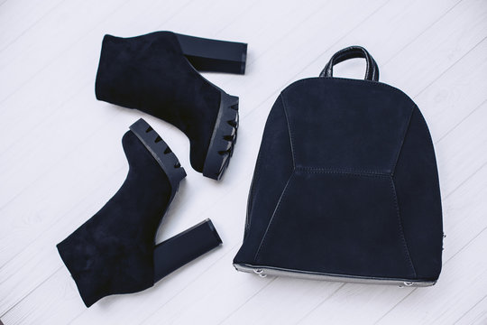 Stylish women's handbag and autumn boots made of black suede leather on a white wooden background