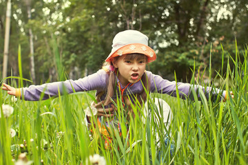 Naklejka na ściany i meble Little cheerful girl playing in the grass