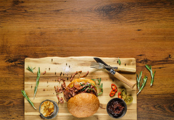 Homemade beef burger with crispy bacon and vegetables on rustic serving board