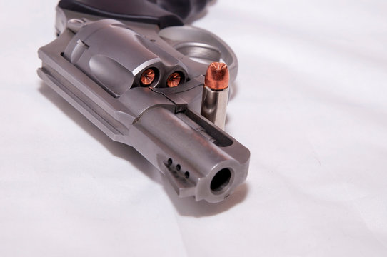 A stainless 357 magnum revolver with a single bullet next to it shown on a white background