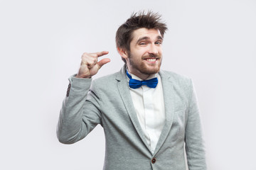 Give me a few more please. Portrait of hopeful handsome bearded man in casual grey suit and blue bow tie standing and looking and camera. indoor studio shot, isolated on light grey background.