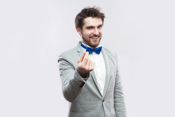 Portrait of funny handsome bearded man in casual grey suit, blue bow tie standing with money...