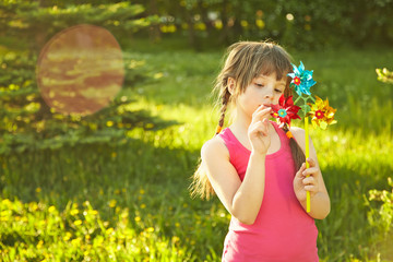 cheerful little girl playing with pinwheel in summer park