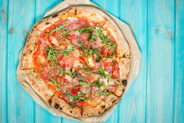 Pizza with prosciutto, arugula and parmesan on blue wooden background. Top view.