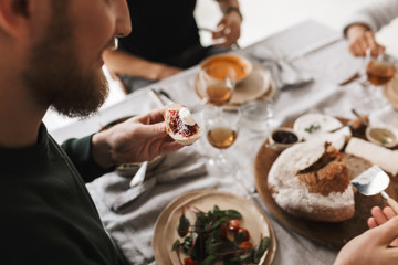 Close up man sitting at the table holding slice of bread with jam and cheese in hand on lunch in...