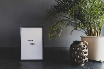 White letter board. Grey wall. Green plant. With the inscription "YOGA TIME".