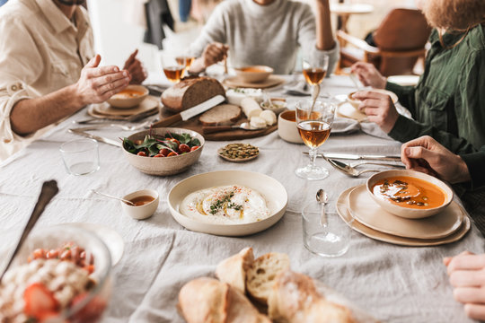 Close up group of young people sitting at the table full of delicious food and glasses of wine having lunch in cafe