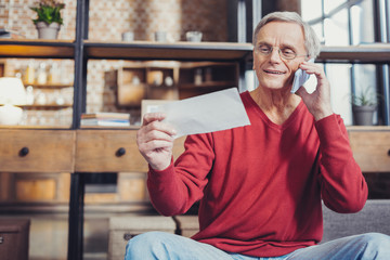 Cheerful pensioner smiling while making a call to a bank