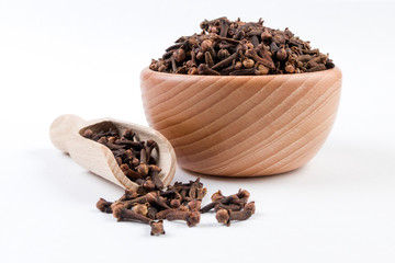 Cloves in wooden bowl and scoop isolated on white background. Closeup.