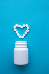 Pills, tablets in the shape of a heart and a white bottle on a blue background.