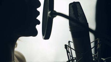 Lovely woman singing into the microphone in the recording studio. Profile of a singer with a beautiful face and lips. Black and white.Close up - Powered by Adobe