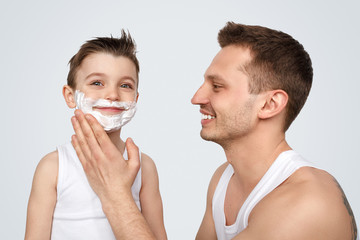 Cheerful father smearing shaving foam on son