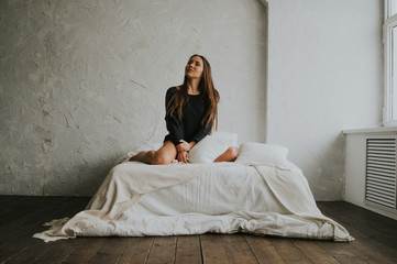 Beautiful tender girl in black lingerie and jumper is sitting on the bed. A young woman basks in...