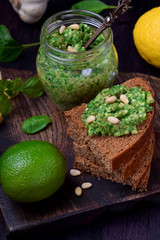 Green pesto in a jar and on a piece of bread surrounded by the ingredients