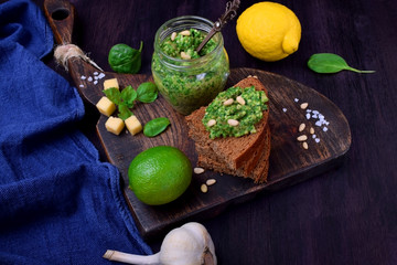 Fototapeta na wymiar Green pesto in a jar and on a piece of bread surrounded by the ingredients