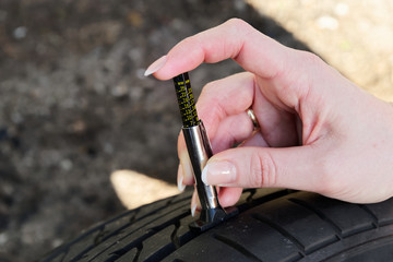 Close-up of woman checking tread on car tyre with gauge