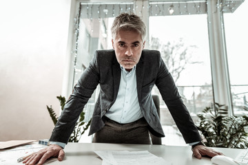 Tall grey-haired adult manager in eyeglasses looking irritated