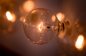 An incandescent light warmly glows.  Reminiscent of a vintage sign, you can see the glowing filament surrounded by soft focus and bokeh. Shot behind-the-scenes of a television production.