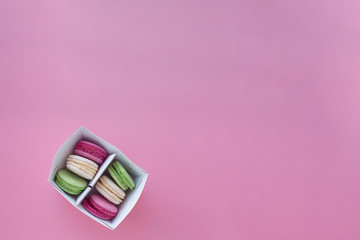 several multi-colored macarons in a paper box on a pink background
