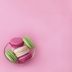 several multi-colored macarons in a glass plate on a square pink background