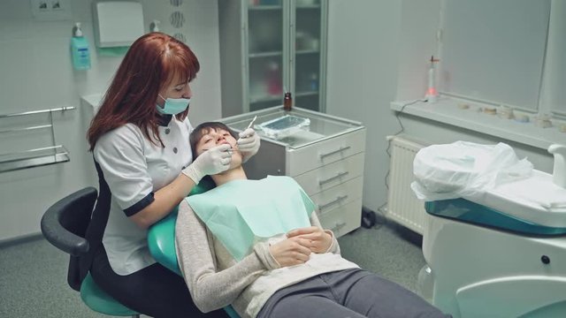 Woman patient on the inspection of the teeth in dentistry. Female dentist treats a girl's teeth in a light clean dental clinic