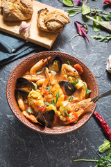 French fish soup Bouillabaisse with seafood, salmon fillet, shrimp, mussels on stone background. Delicious dinner