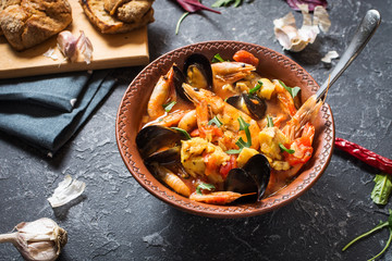 French fish soup Bouillabaisse with seafood, salmon fillet, shrimp, mussels on stone background. Delicious dinner