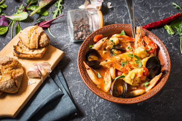 French fish soup Bouillabaisse with seafood, salmon fillet, shrimp, mussels on stone background....