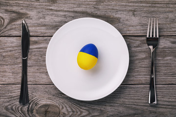 Easter egg, painted in the color of the Ukrainian flag on a plate with cutlery, top view