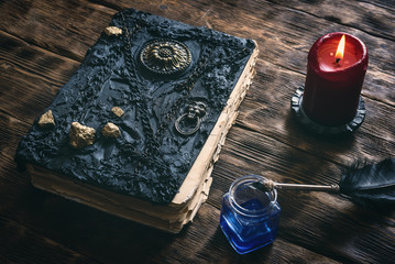 Ancient magic book, ink well and a quill pen on a wooden table background. Spell book.