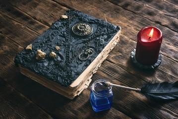 Ancient magic book, ink well and a quill pen on a wooden table background. Spell book.