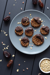 Raw vegan gluten free cookies with chocolate glaze served with ingredients: oats, dates and himalayan salt on grey plate