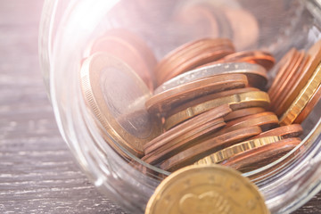 Euro coins in transparent beacon on a black wooden table.