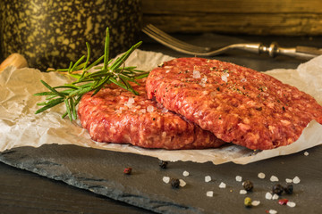 Raw burger beef patty with rosemary and garlic on dark cooking background 