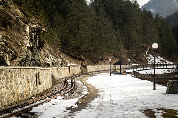 Narrow gauge railway track through forest with beautiful nature, stone, mountain. Snow melting in end of winter. 