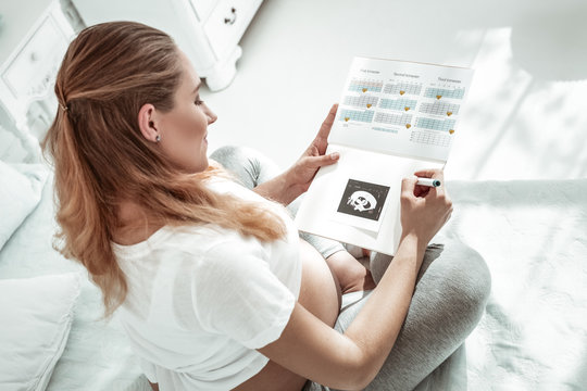 Focused pleasant future mother adding ultrasound photo in dairy