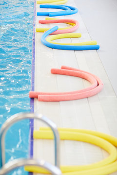 Background image of colorful pool noodles laying by water in public swimming pool, copy space